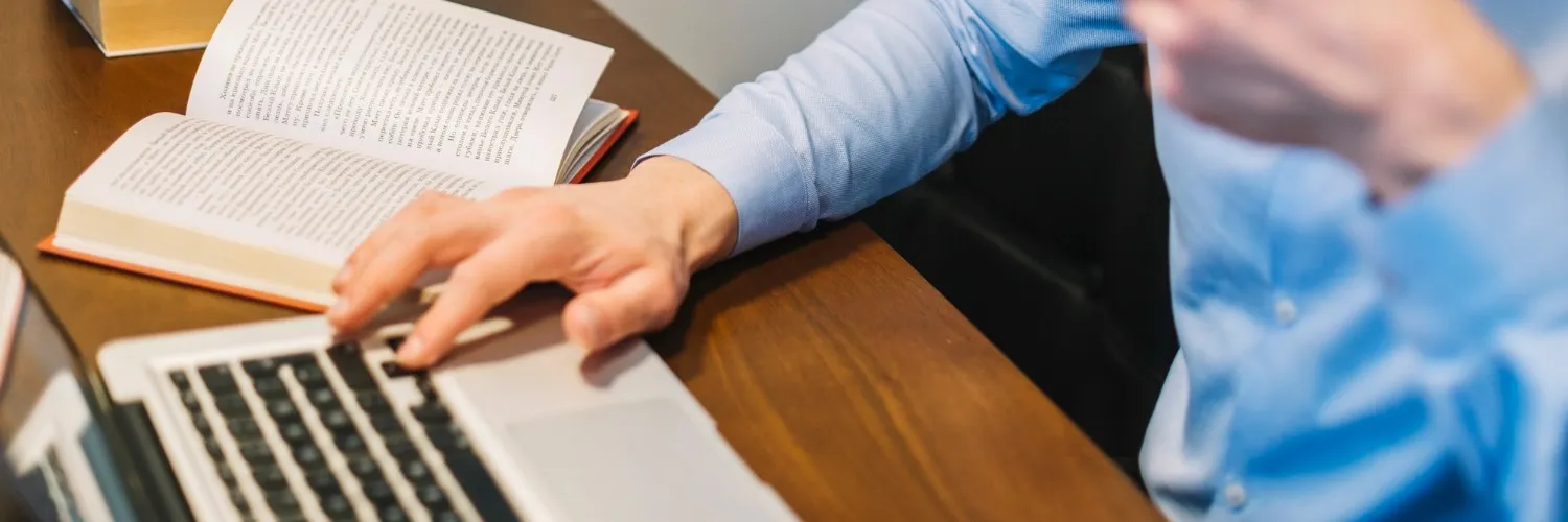 Profissional de tradução trabalhando em um projeto com auxílio de computador e material impresso, simbolizando a importância do toque humano na tradução